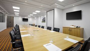 A conference room with a long table, chairs, a projector screen, and a wooden cabinet.