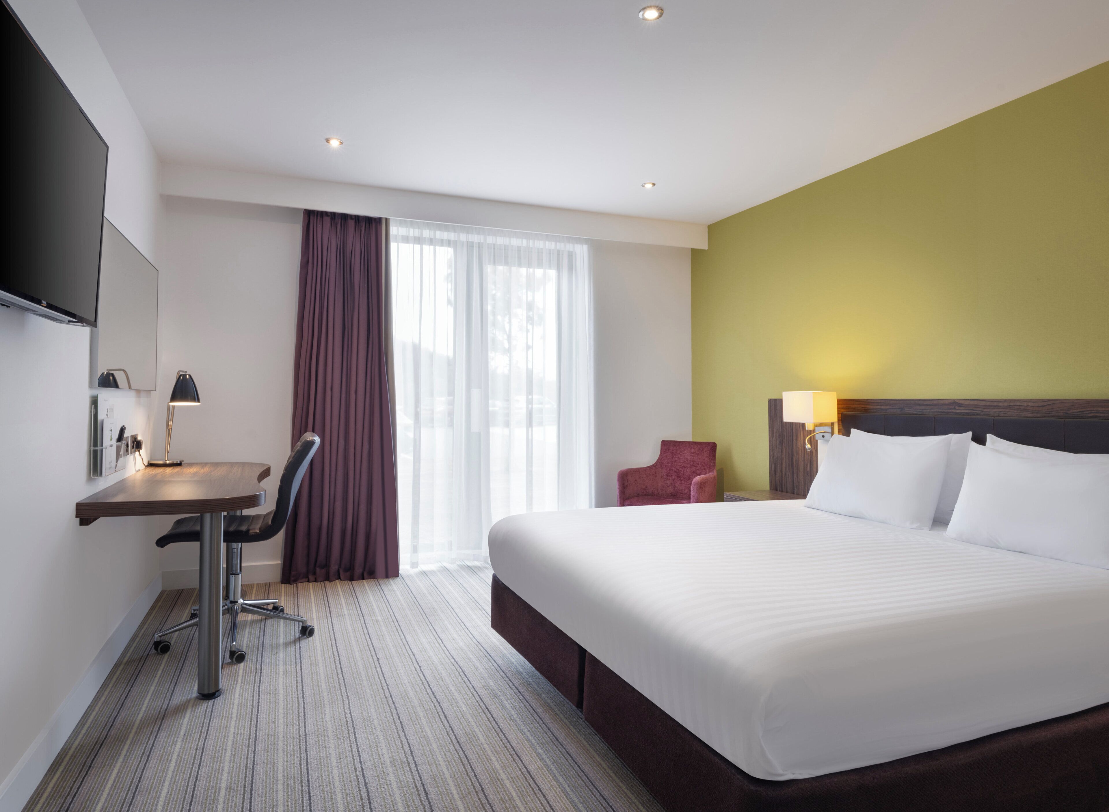 A hotel room with a bed, desk, chair, and a TV mounted on the wall.