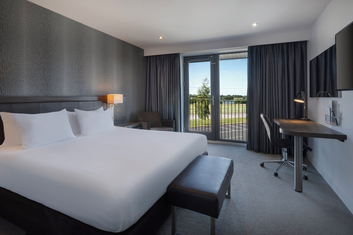 A modern hotel room with a large bed, a desk, and a view of a tennis court.
