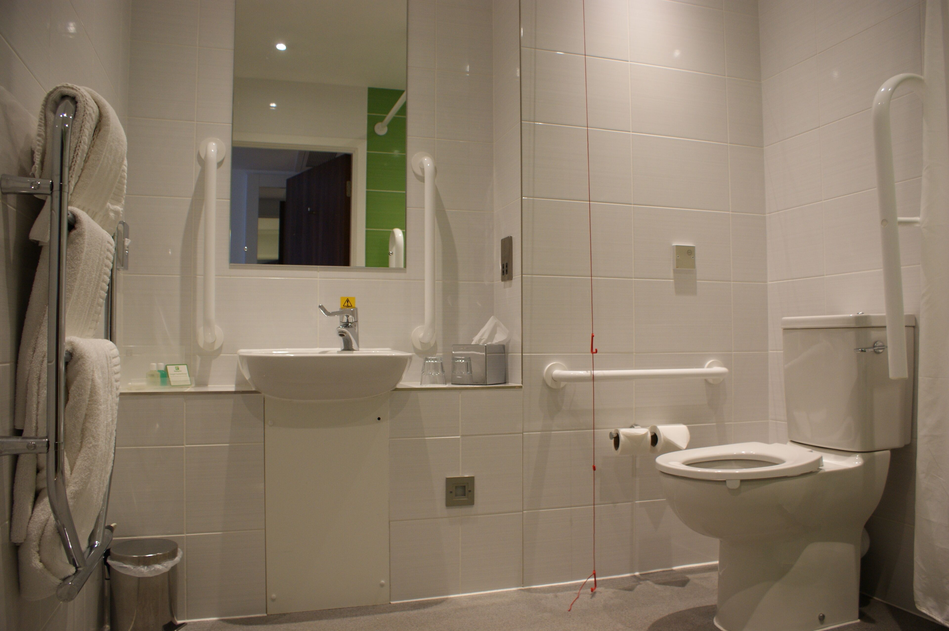 A modern bathroom with a sink, toilet, and handrails.