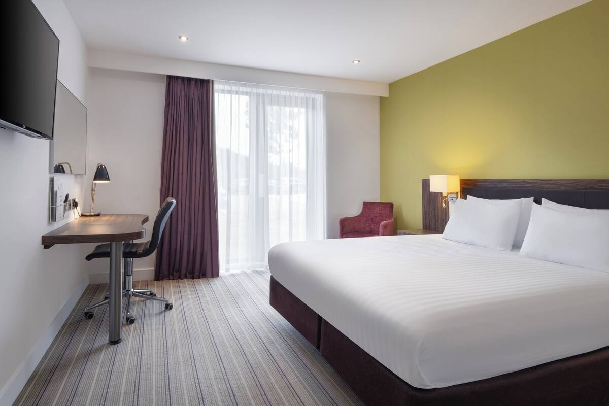 A hotel room with a bed, desk, chair, and a TV mounted on the wall.