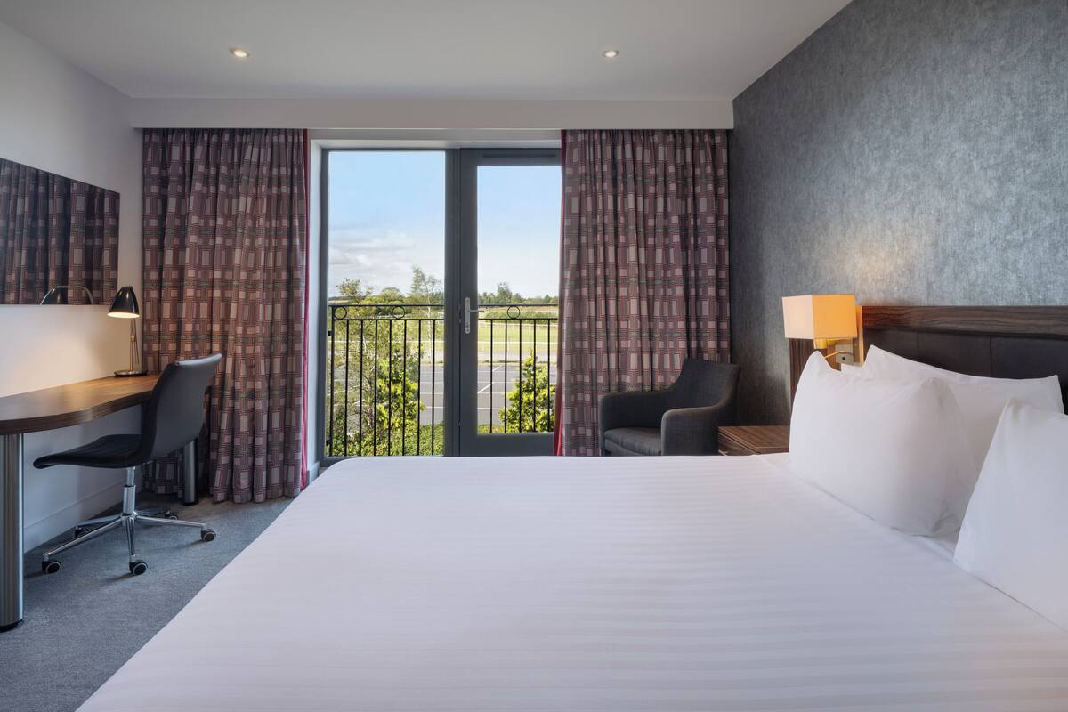 A hotel room with a bed, desk, chair, and a view of the outdoors.