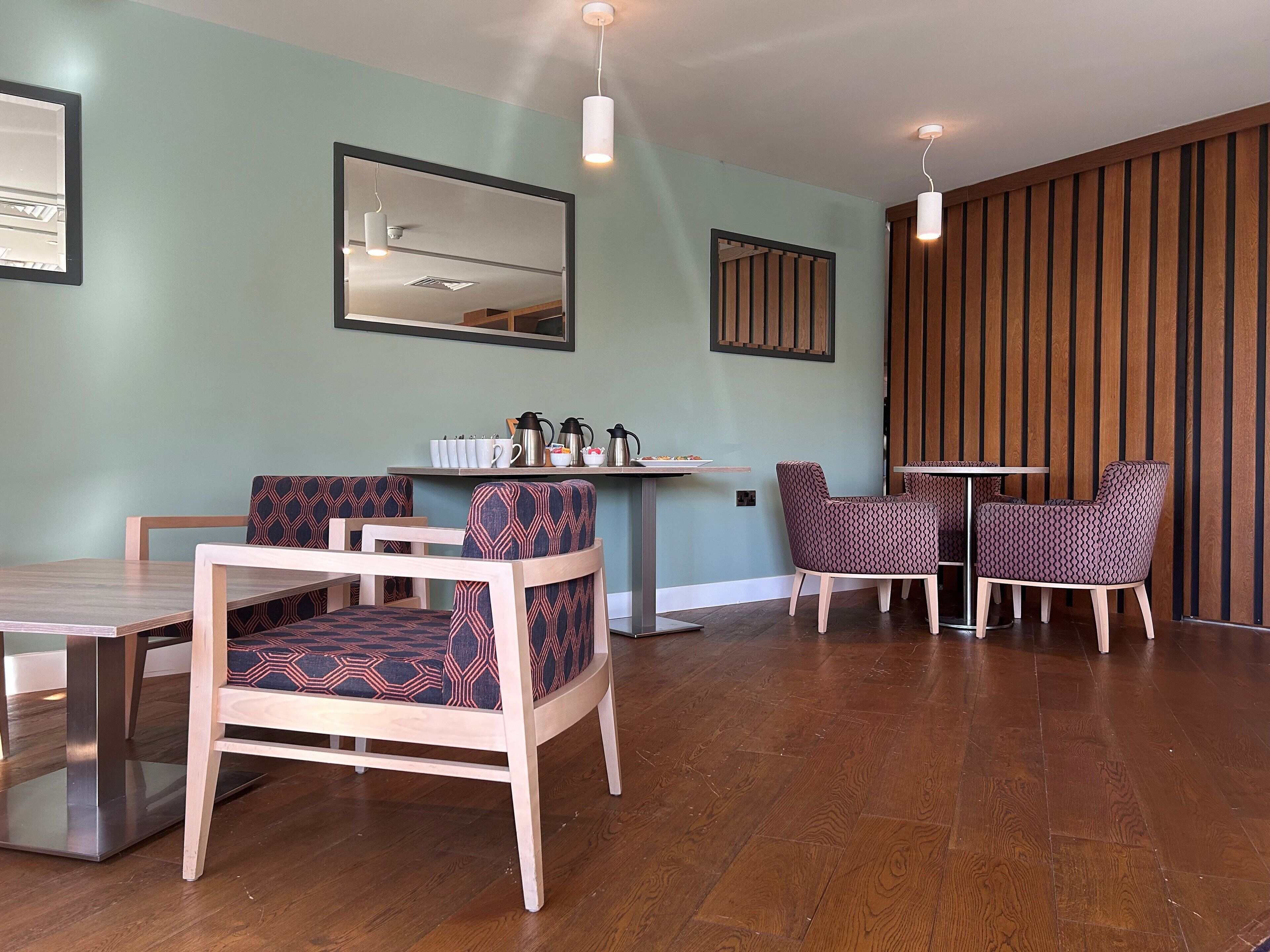 A modern dining area with wooden flooring, patterned chairs, a central table, and a wall-mounted shelf with kitchenware.