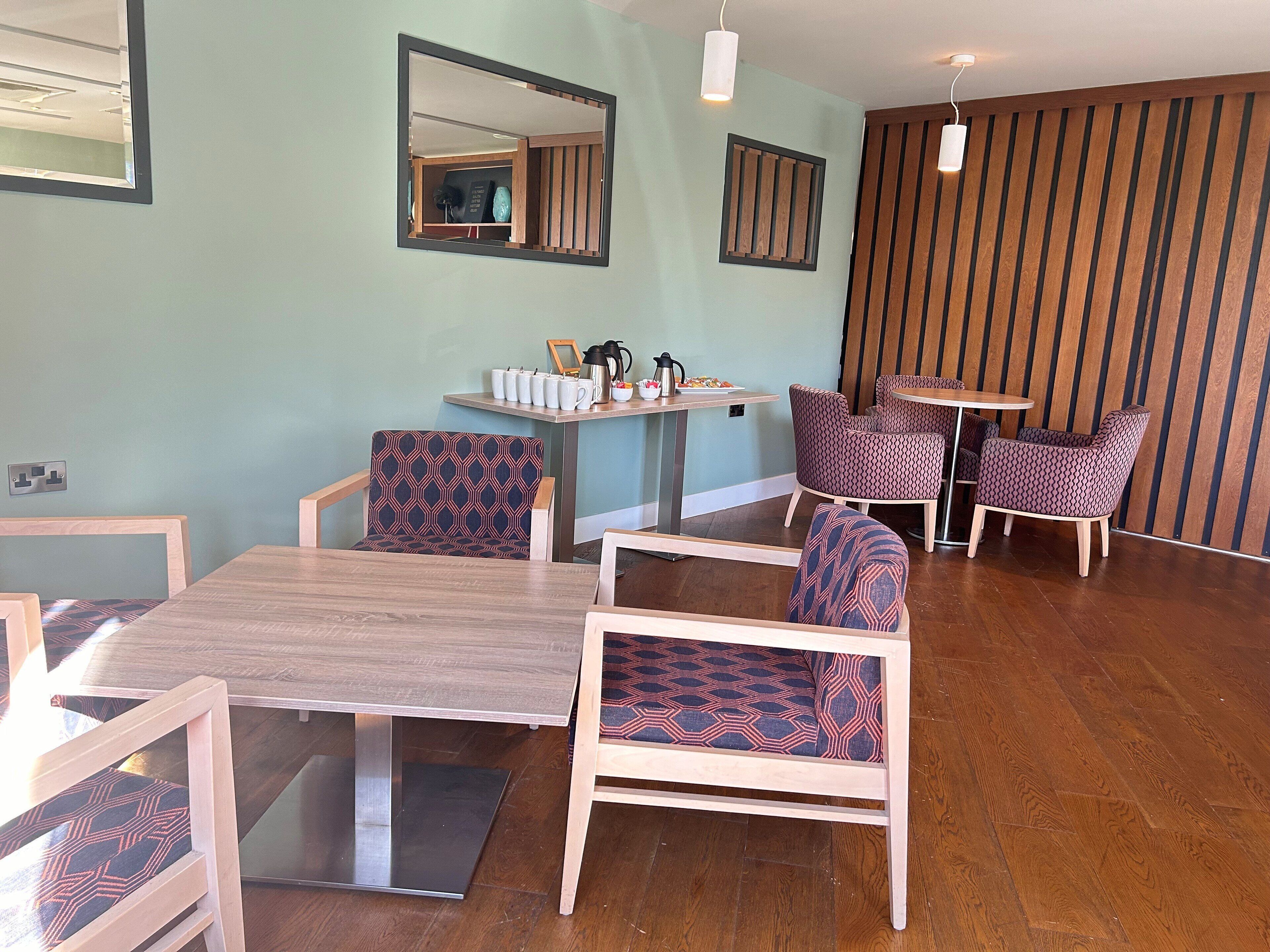 A dining area with a wooden table and chairs, a small round table with a coffee pot, and a wall-mounted mirror.
