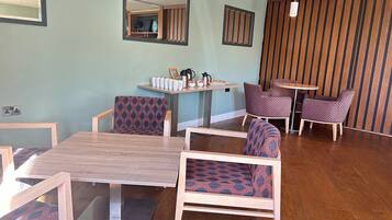 A dining area with a wooden table and chairs, a small round table with a coffee pot, and a wall-mounted mirror.
