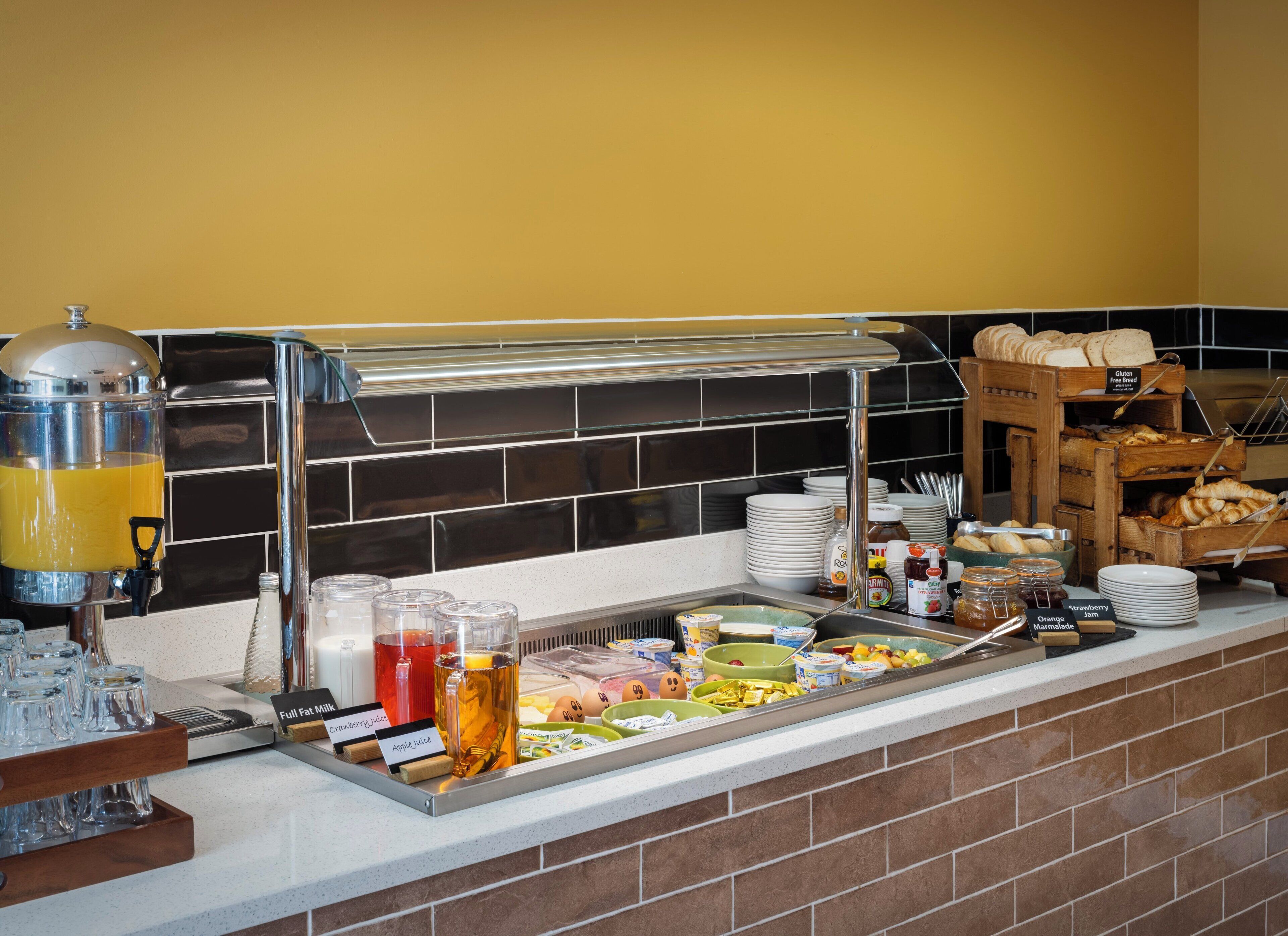 Een buffet met diverse etenswaren en drankjes, waaronder een jusdispenser, borden en een broodpresentatie.