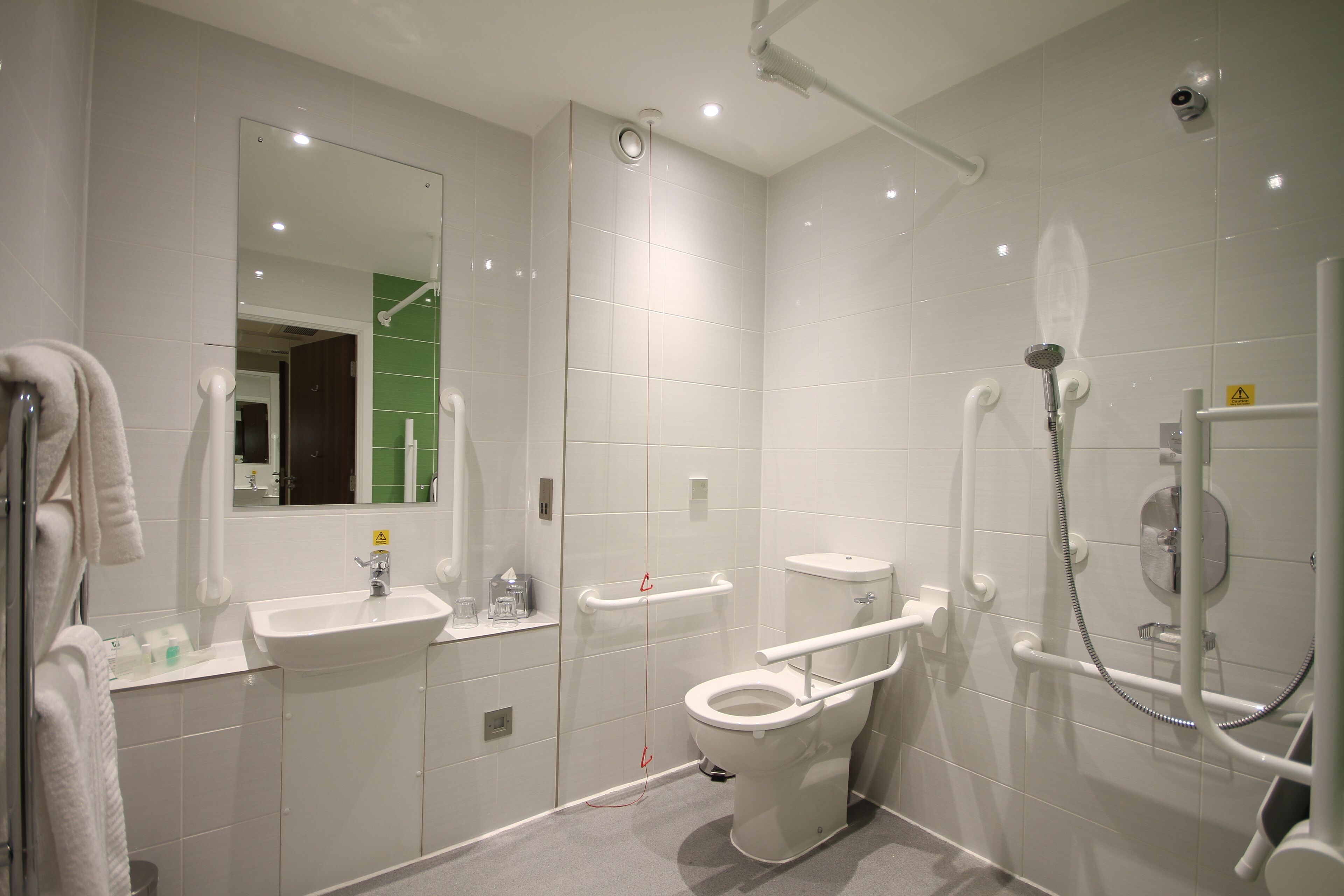 A modern bathroom with a white sink, toilet, and shower area, including grab bars and a handheld showerhead.