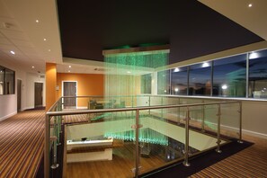 A hotel lobby with a glass railing, a staircase, and a decorative hanging light fixture. - Holiday Inn Huntingdon - Racecourse by IHG (Huntingdon)
