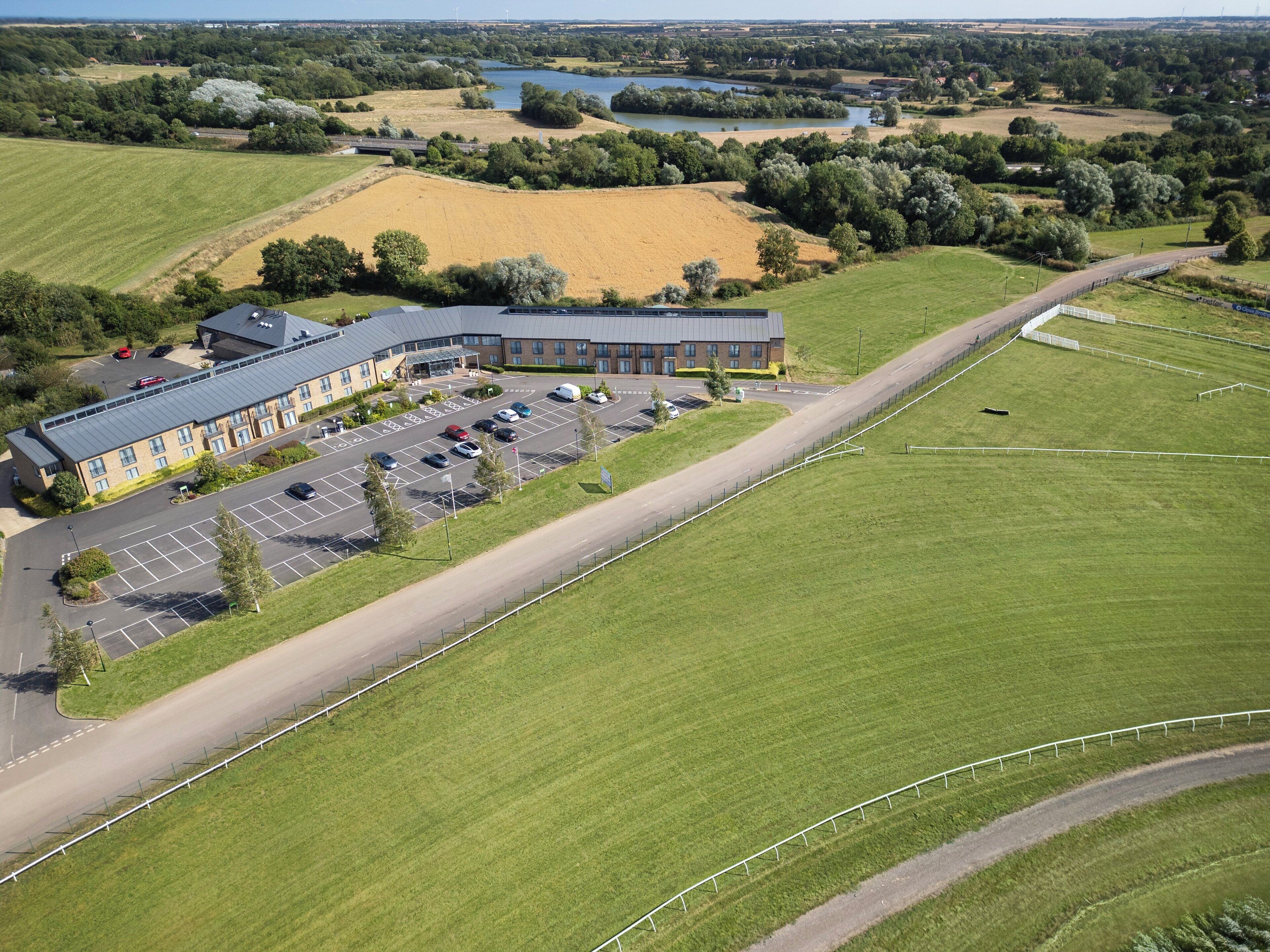 An aerial view of a building with a parking lot and adjacent green fields.