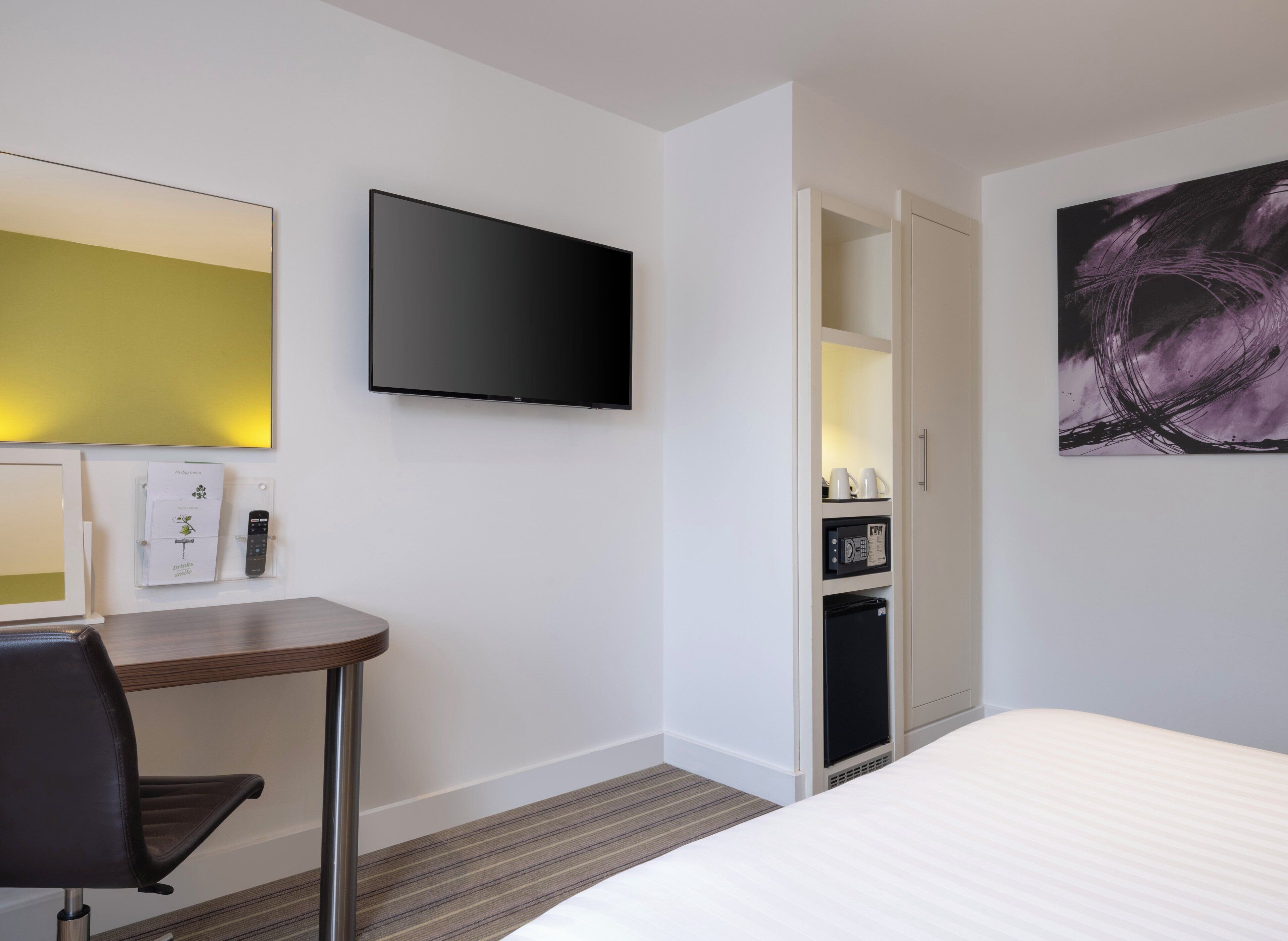 Une chambre d’hôtel comprenant un lit, un bureau avec une chaise, un téléviseur à écran plat, un minibar et un tableau au mur.
