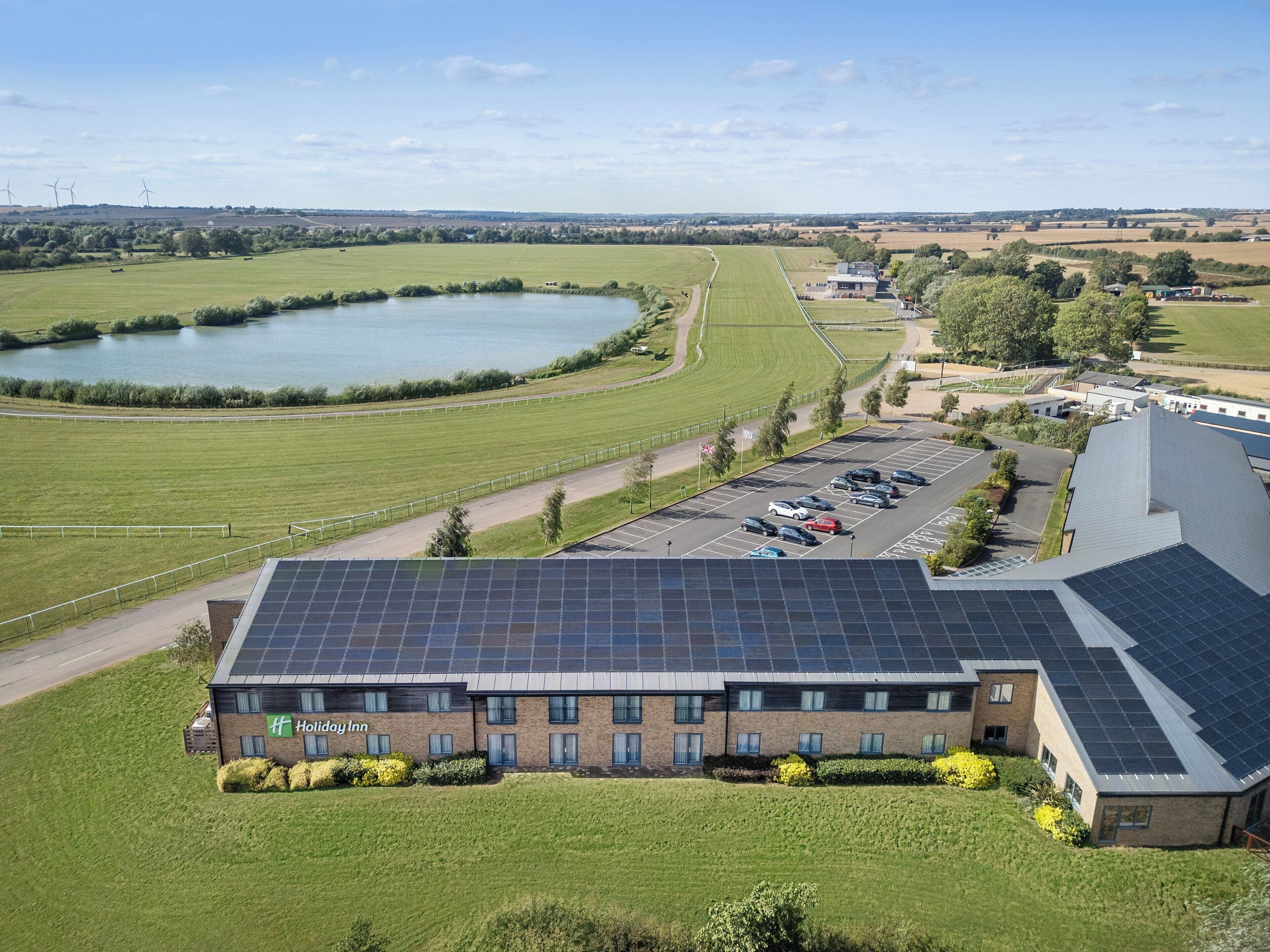 A Holiday Inn with solar panels, a parking lot, and a view of a lake and fields.