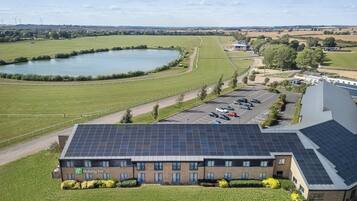 A Holiday Inn with solar panels, a parking lot, and a view of a lake and fields.