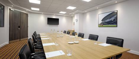 A conference room with a long table, chairs, a TV, and a clock on the wall.