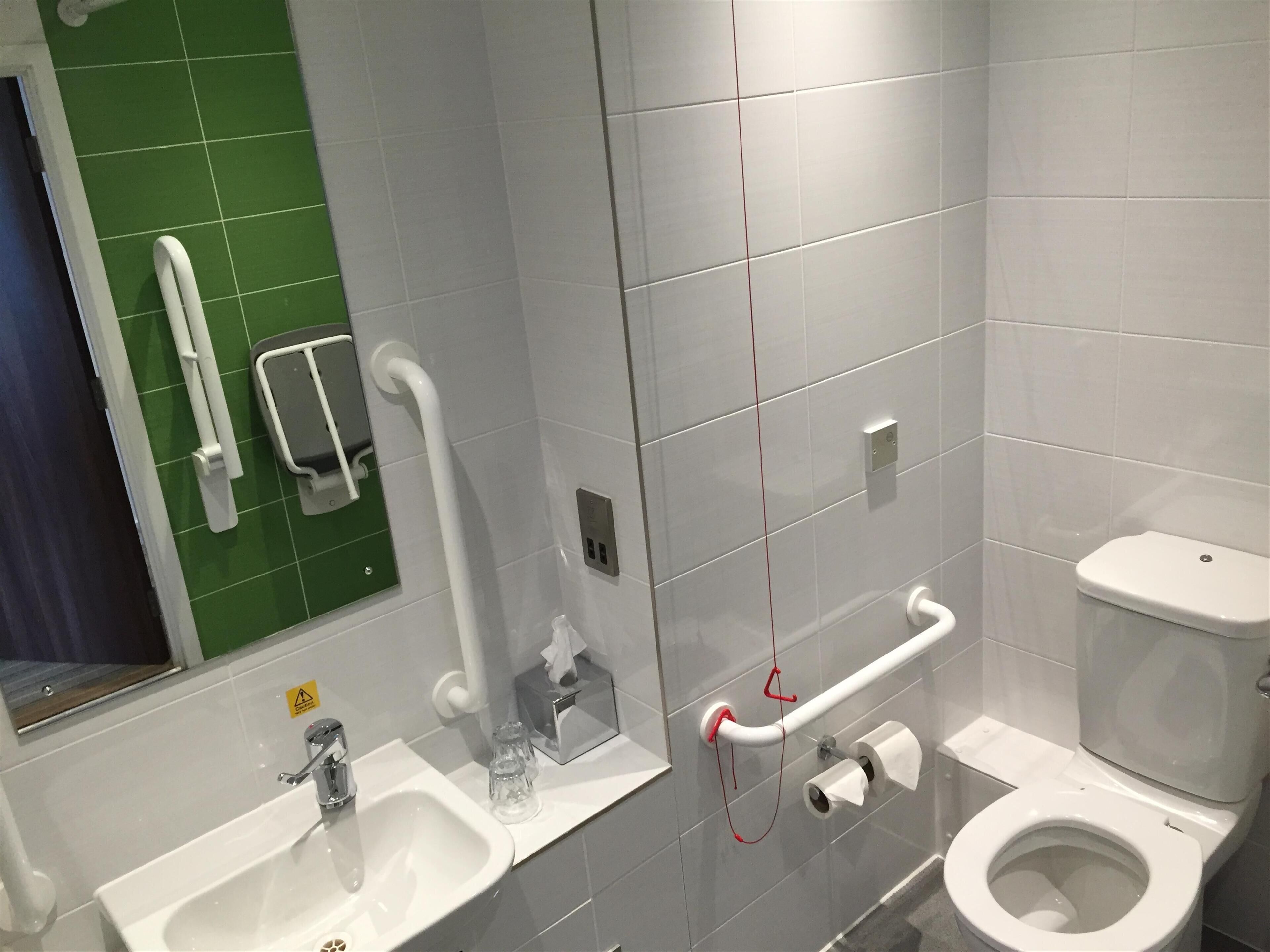 Un baño moderno con lavamanos, inodoro y barras de apoyo.