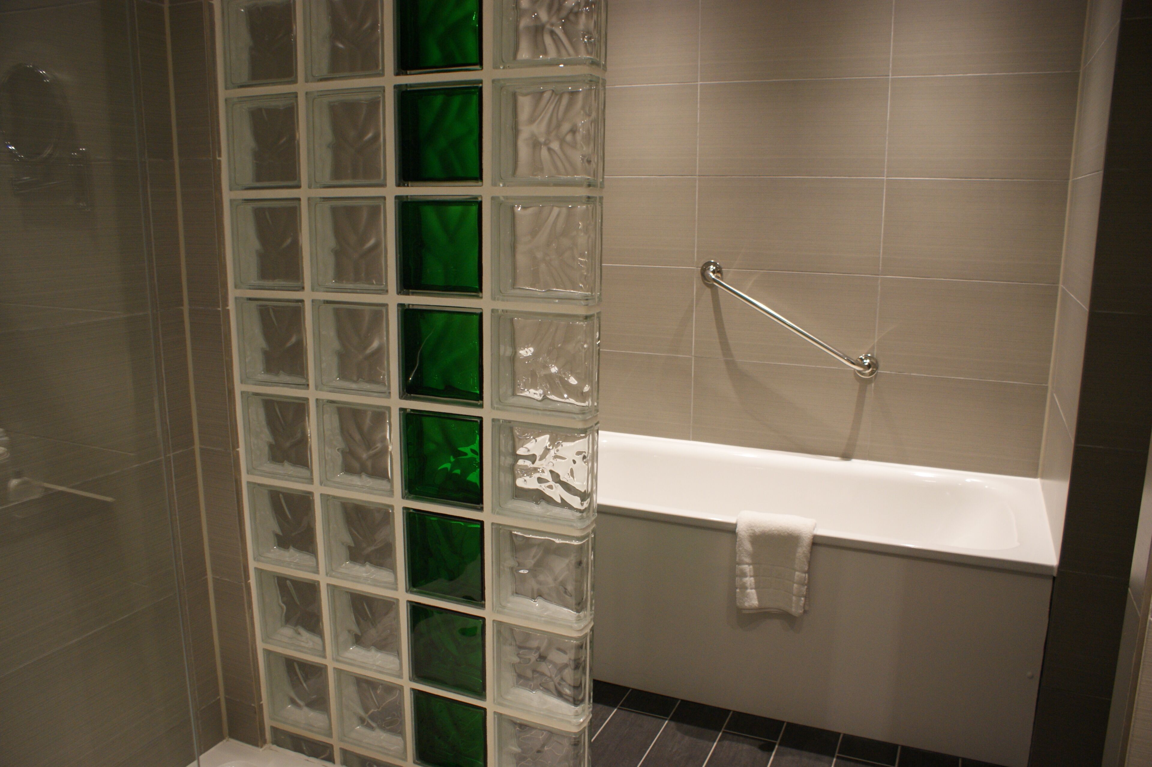 A bathroom with a glass block partition, a white bathtub, and a towel rack.