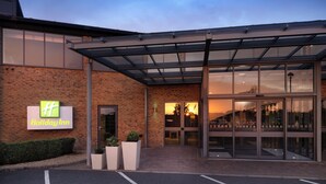 A Holiday Inn with a brick facade, large glass entrance, and a covered outdoor area. - Holiday Inn Huntingdon - Racecourse by IHG (Huntingdon)