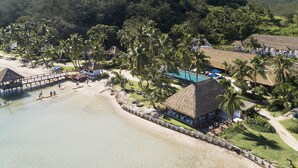 Een tropisch resort met een strand, hutten met rieten daken en een zwembad.