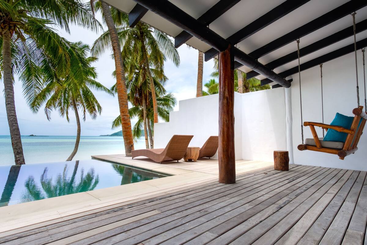 Eine Holzterrasse mit Pool, Liegestühlen und einer Hängematte mit Blick auf den Ozean.