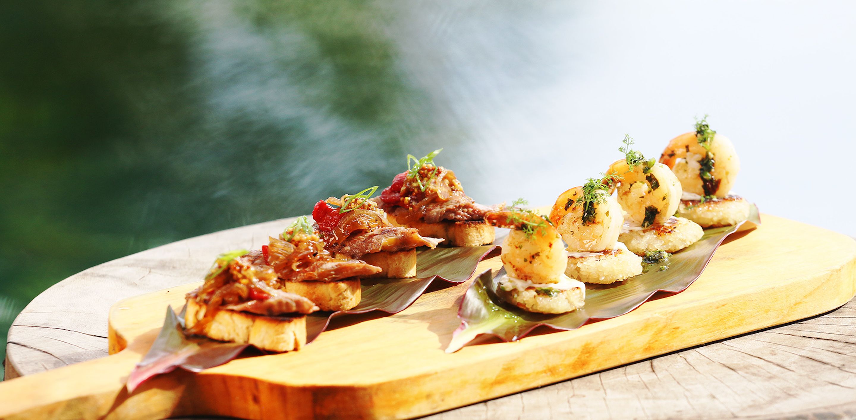 Una tabla de madera con alimentos, probablemente una comida o aperitivo, sobre una mesa con un fondo verde desenfocado.