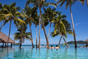 A clear blue pool surrounded by palm trees and a thatched-roof structure. - Tropica Island Resort - Adults Only (Malolo Island)