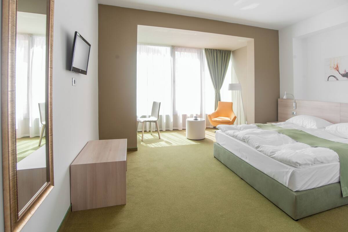 A hotel room with a bed, a desk, a chair, and a window with curtains.