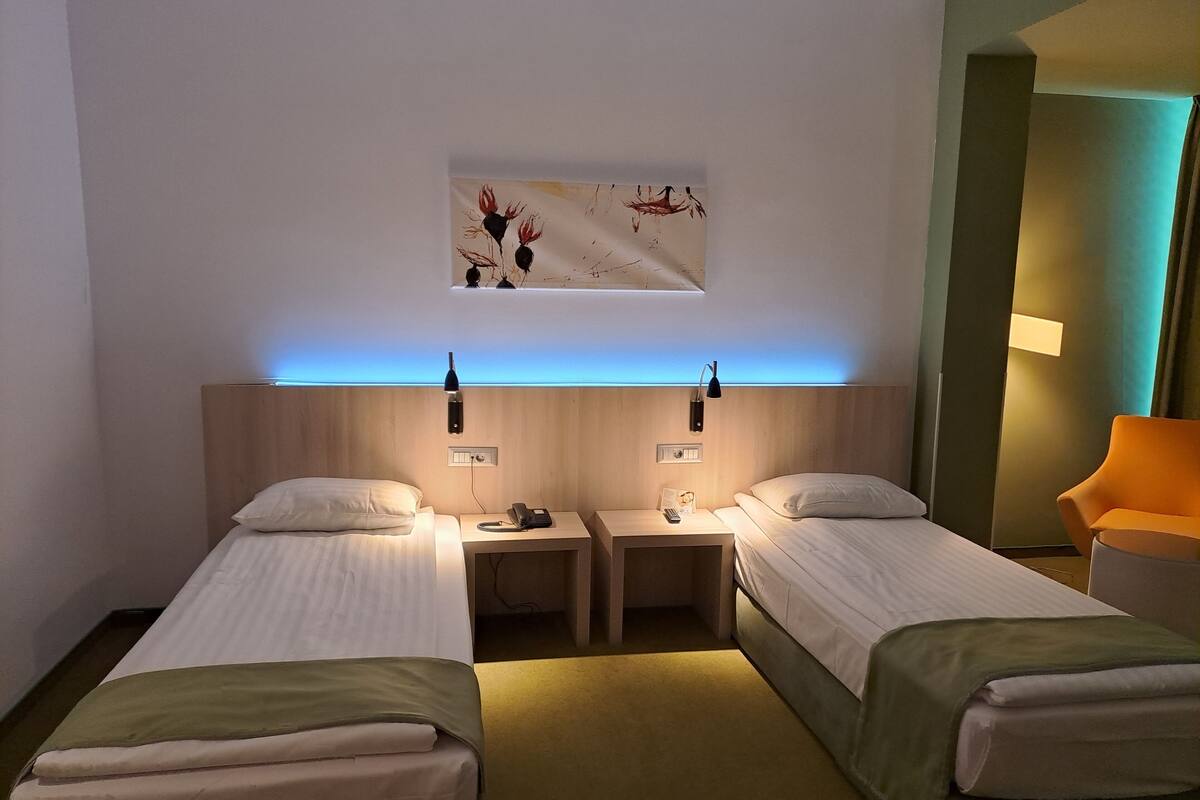 A hotel room with two single beds, a nightstand with a phone and remote, a wall-mounted artwork, and a small table lamp.