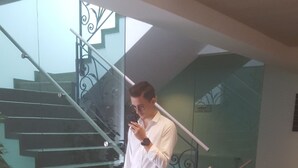 Una persona de pie en una escalera con barandilla de vidrio, sosteniendo un teléfono.