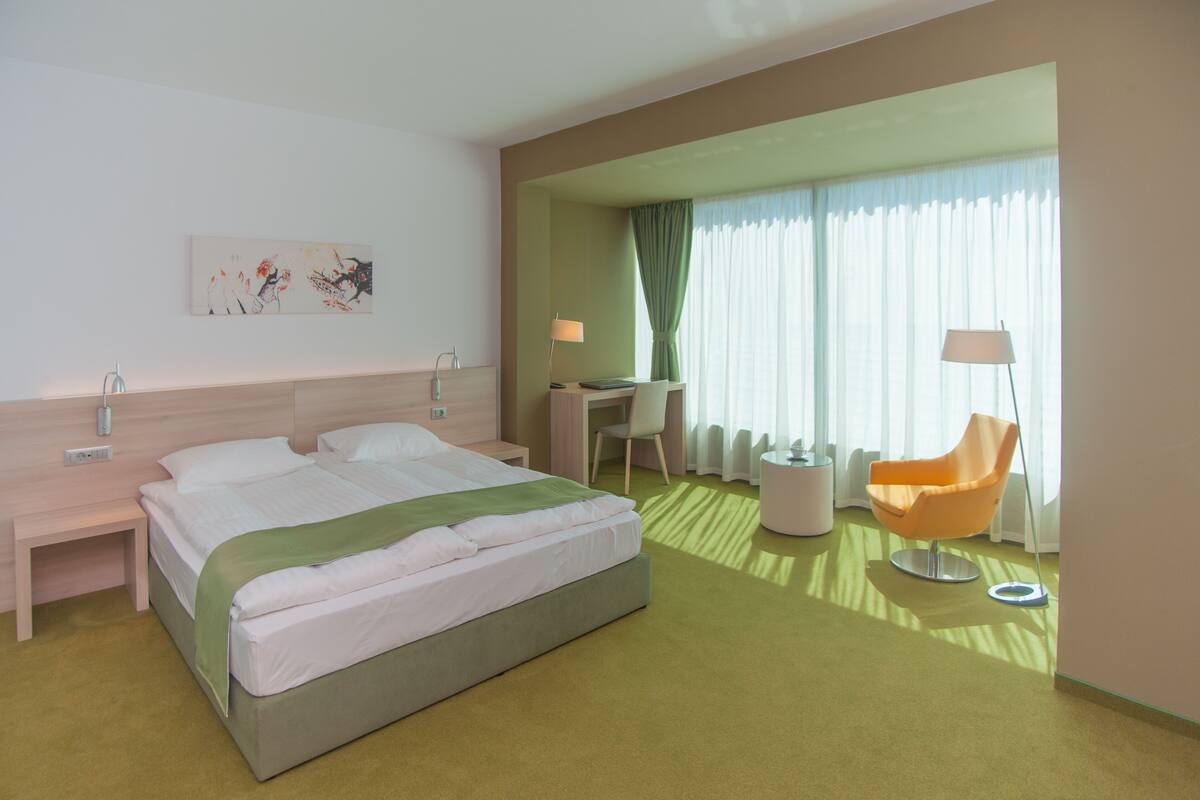 A hotel room with a bed, a desk, a chair, and a painting on the wall.