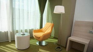 Habitación de hotel con un sillón naranja moderno, una pequeña mesa blanca con una taza, una lámpara de pie y un banco de madera.