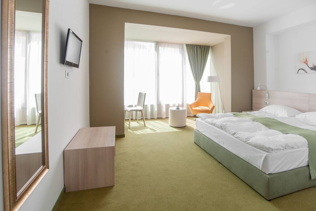 A hotel room with a bed, a desk, a chair, and a window with curtains.