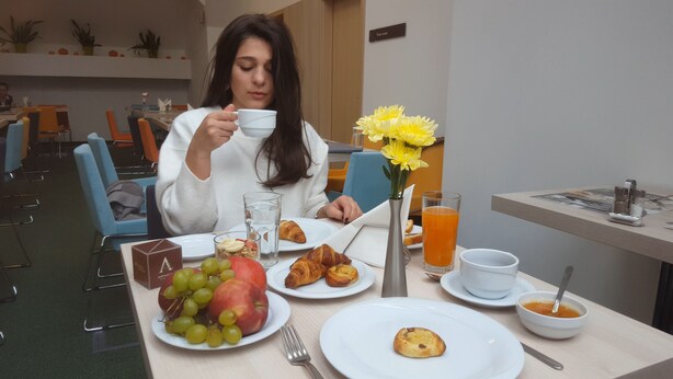 Desayuno preparado para dos personas, con platos de fruta, croissants y un vaso de jugo de naranja.