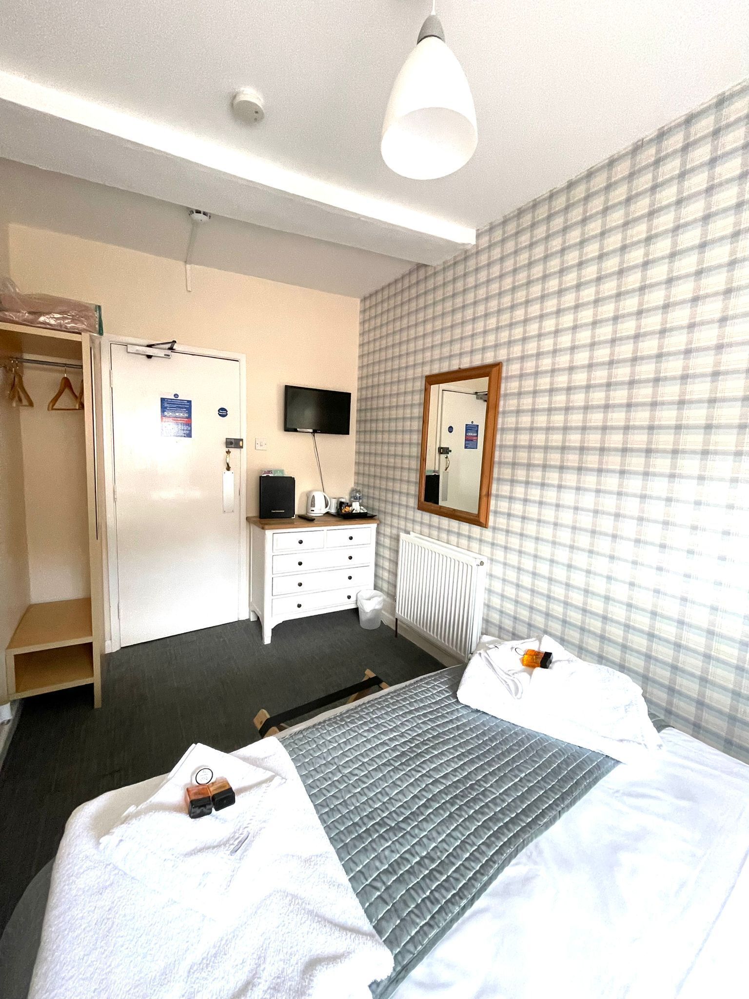 A hotel room with a bed, a dresser, a mirror, a television, and a wardrobe.