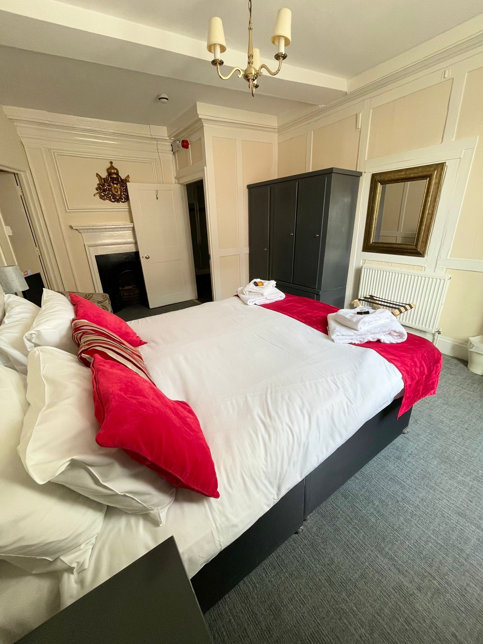 A large bed with white and red bedding, a black wardrobe, a chandelier, and a fireplace.