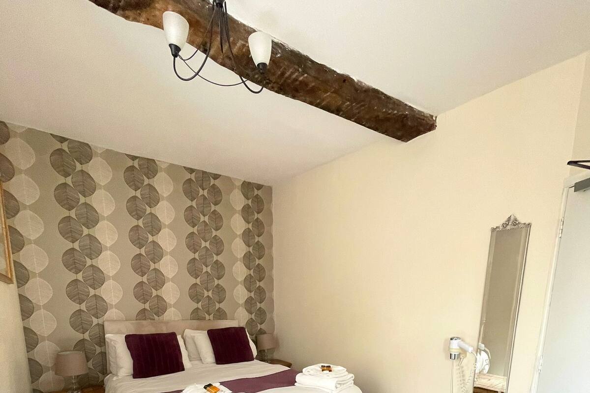 A bedroom with a bed, bedside tables, a wooden stool, a mirror, and a ceiling light fixture.