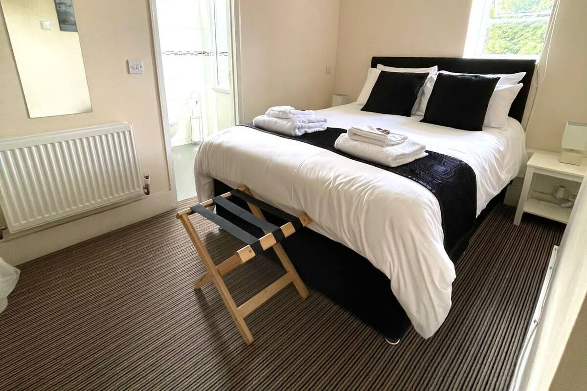 A hotel room with a bed, a radiator, a window, and a door.