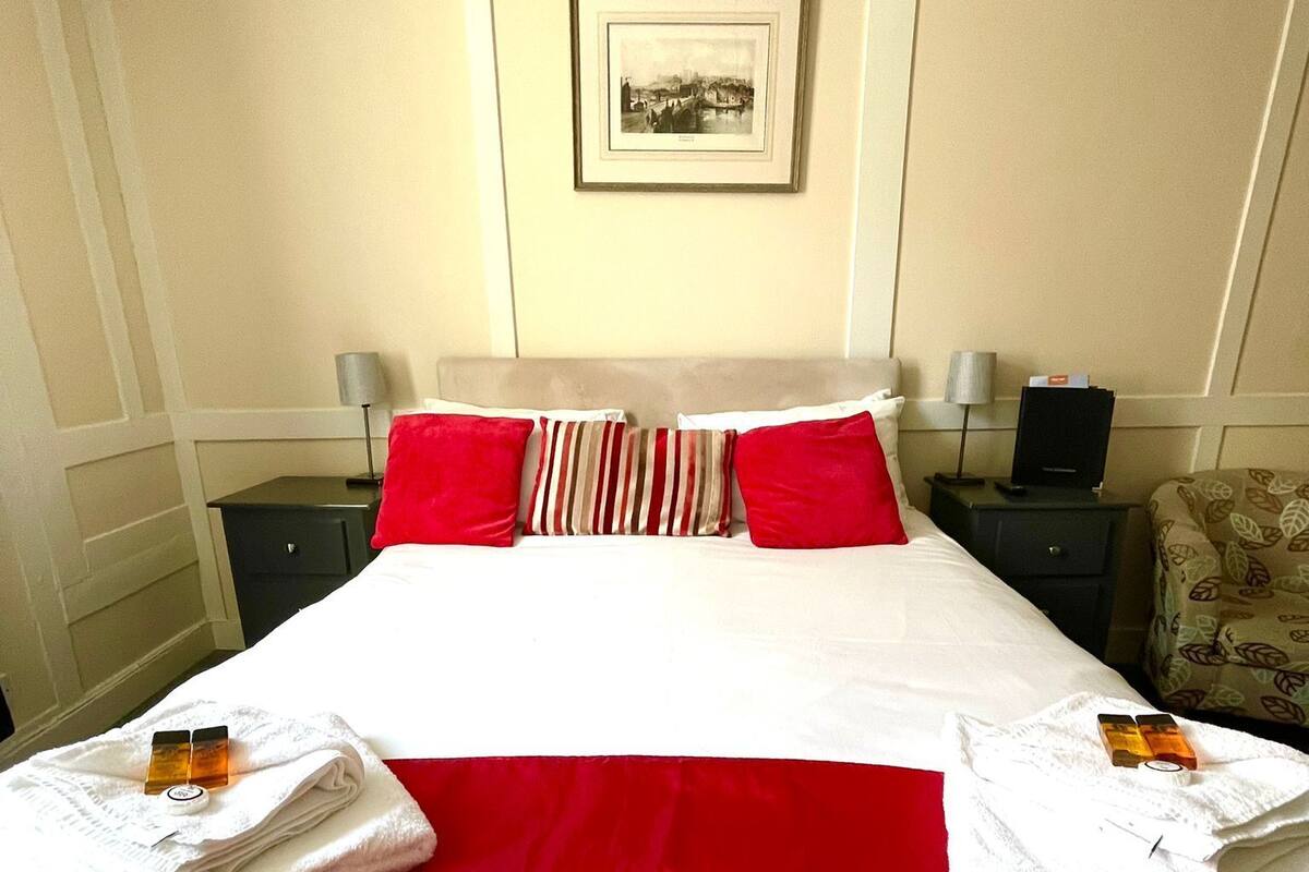 A hotel room with a large bed, red and white bedding, two nightstands with lamps, a framed picture on the wall, and towels on the bed.