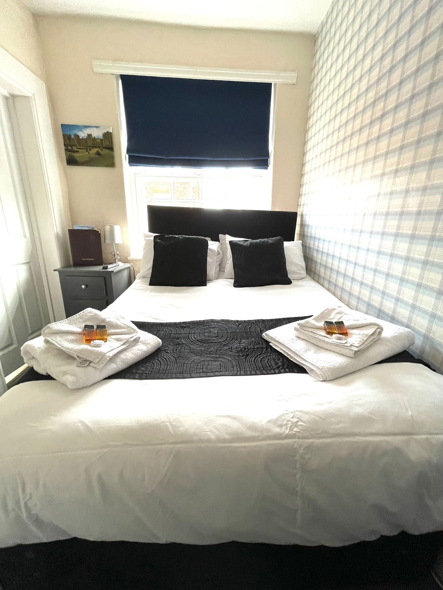Een hotelkamer met een groot bed, twee kussens, een nachtkastje met een lamp en een raam met uitzicht.