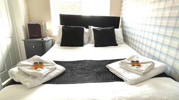 Een hotelkamer met een groot bed, twee kussens, een nachtkastje met een lamp en een raam met uitzicht.