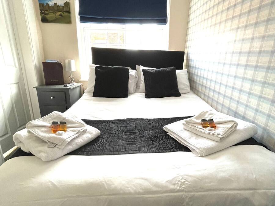 Een hotelkamer met een groot bed, twee kussens, een nachtkastje met een lamp en een raam met uitzicht.