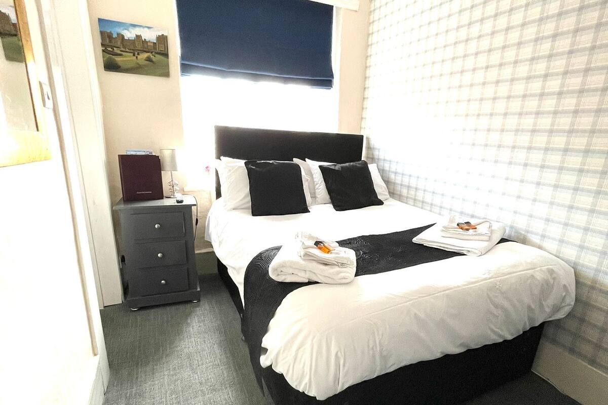 A neatly arranged hotel room with a bed, a nightstand, a lamp, and a view of the city through the window.