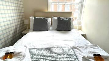 A hotel room with a neatly made bed, a window with a view of buildings, and a checkered curtain.