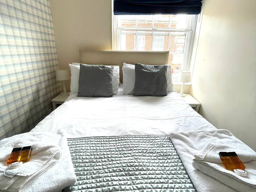 A hotel room with a neatly made bed, a window with a view of buildings, and a checkered curtain.