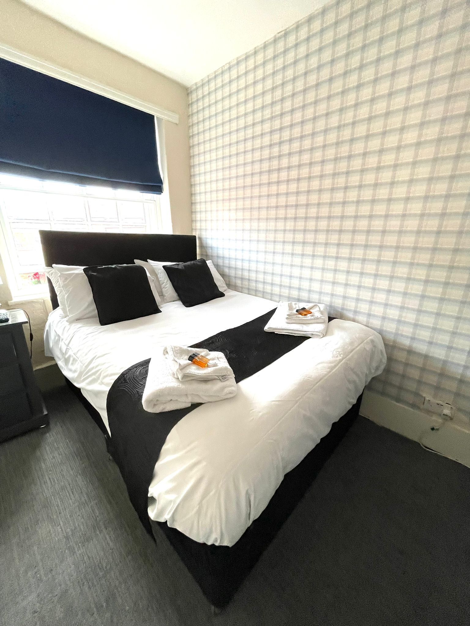 A hotel room with a neatly made bed, a bedside table, and a window with a view.
