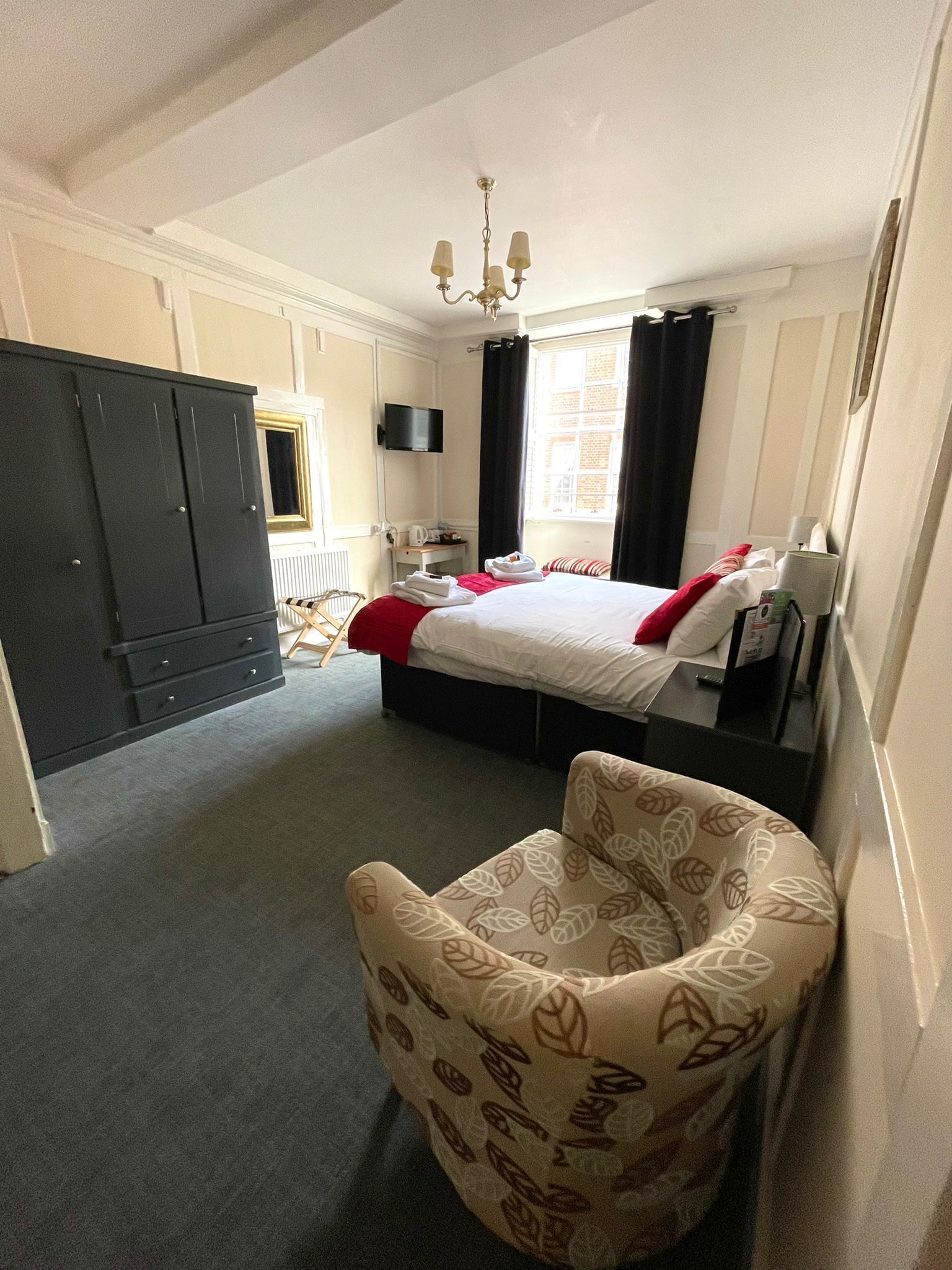 Una habitación de hotel con cama, una silla, un escritorio, televisor y armario.
