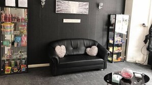 A black leather sofa with heart-shaped cushions, a glass coffee table, a wall clock, a framed abstract artwork, and a glass display case with various items. - The Butterfly Hotel - Group Weekends (Blackpool)