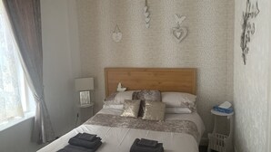 A neatly made bed with pillows and a blanket, a bedside table with a lamp, and decorative wall art. - The Butterfly Hotel - Group Weekends (Blackpool)