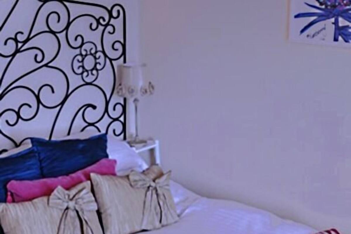A bedroom with a metal headboard, a bedside table with a lamp, and multiple pillows.