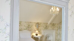 A bedroom with a large mirror, a bed, a nightstand with a lamp, and a fireplace. - The Mount Somerton (Somerton)