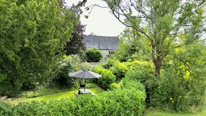 A well-maintained garden with a wooden bench and a black umbrella, surrounded by lush greenery and a stone building in the background. - The Mount Somerton (Somerton)