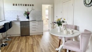 A modern kitchen with white cabinets, a dishwasher, and a dining area with a round table and two chairs. - The Mount Somerton (Somerton)